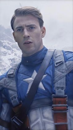 a man dressed as captain america standing in front of snow covered mountains with his hands on his hips