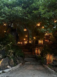 a stone path leading up to a building with lit lanterns on the trees above it