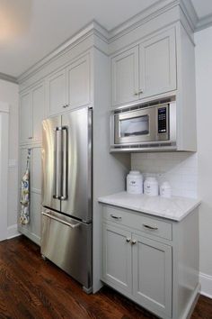 a stainless steel refrigerator in a white kitchen with wood floors and cabinets on both sides