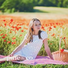 a woman sitting on a blanket in the middle of a field with red poppies