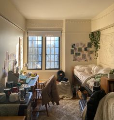 a dorm room with two beds, desks and other items on the floor in front of large windows