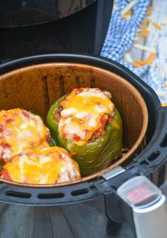 three stuffed peppers in an air fryer with the lid open and some cheese on top