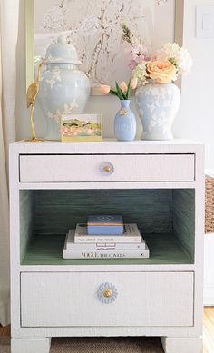 a nightstand with two vases on top of it next to a painting and flowers