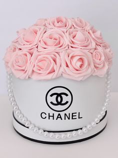 a chanel hat with pink roses and pearls around the top is shown on a white table