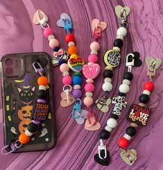 a cell phone case with some charms attached to it on a purple surface next to an assortment of keychains