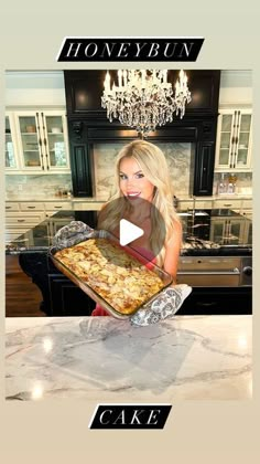 a woman holding a tray of food on top of a kitchen counter next to a chandelier