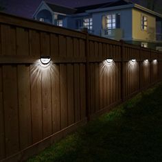 three lights on the side of a wooden fence at night with houses in the background