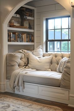 a white couch sitting under a window next to a book shelf