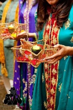 two women in colorful outfits holding small baskets with sushi on them and one woman wearing a blue dress