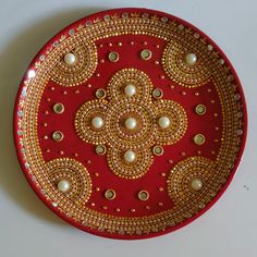 a red and gold plate with pearls on the edge, sitting on a white surface