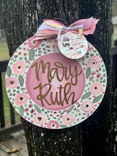 a pink and green plate hanging from a tree with the words mary ruth on it