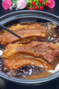 some meat is being cooked in a pot with chopsticks on the table next to it