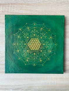 a green and gold painting on wood with an image of a flower of life in the center