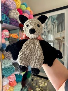 a hand holding up a small stuffed animal in front of a wall of crocheted yarns