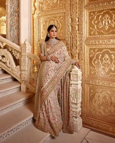 a woman in a white and gold sari standing on stairs with her hand on the railing