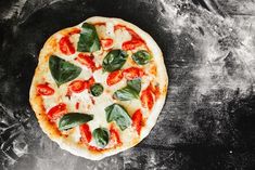 a pizza with tomatoes, basil and cheese on a black background top view from above