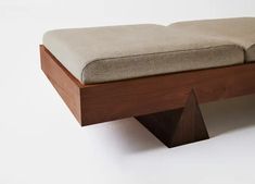 a bench made out of wood and fabric with a cushion on the top, sitting in front of a white wall