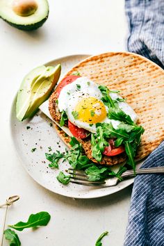 an egg is on top of a sandwich with avocado next to it and a fork