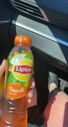 a person holding a bottle of orange juice in their hand while sitting in the back seat of a car