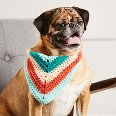 a dog sitting on a chair wearing a crocheted triangle scarf with his tongue hanging out