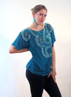 This is a gorgeous 80s vintage beaded and sequined silk top! It is a rich teal ocean green shade with an elaborate floral and swirl design on the front made with iridescent green sequins, metallic bugle beads and faux pearl beads. Shimmering green bugle beads create an allover squiggle design on the rest of the front, the back and the sleeves. It has short sleeves edged with beadwork, a straight hem with bead trim, and large shoulder pads which could be removed, if desired. The top is fully line Luxury Turquoise Festive Blouse Piece, Vintage Beaded Tops For Party, Semi-stitched Sequined Silk Blouse, Vintage Beaded Fitted Tops, Fitted Vintage Sequin Blouse, Ocean Green, Iridescent Green, Green Sequins, Beaded Top