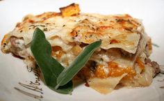 a white plate topped with lasagna covered in cheese and sage leafy garnish