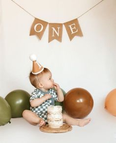 a baby sitting on the floor with a cake in front of him and some balloons