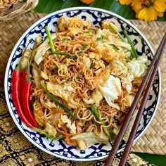 a bowl filled with noodles and vegetables next to two chopsticks on a table