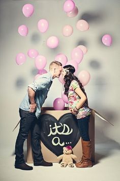 a man and woman kissing in front of a box with balloons floating from it on the ground