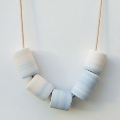 a white and blue necklace hanging from a string on a wall next to a wooden bead