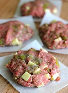 three hamburger patties with cheese and pickles on top are sitting on wax paper