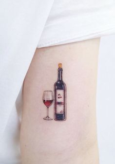 a woman's arm with a bottle and wine glass tattoo on it