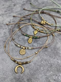 five different necklaces with gold and green beads on a gray surface, one has a crescent