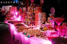 an assortment of candy and candies on display at a party or event with pink lighting