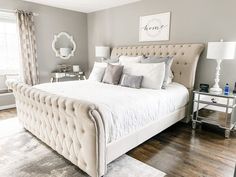 a large white bed sitting in a bedroom on top of a hard wood floor next to a window