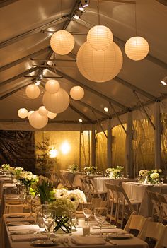 a room filled with tables covered in white tablecloths and paper lanterns hanging from the ceiling