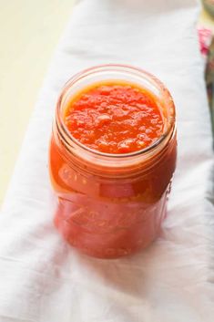 a jar filled with sauce sitting on top of a white table cloth next to a spoon