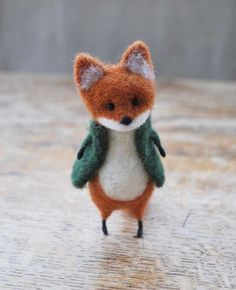 a small toy fox with a green jacket on it's back and eyes closed