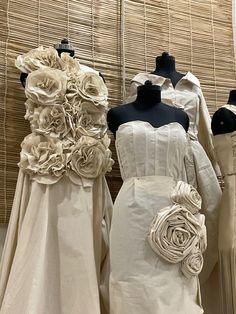 three mannequins dressed in wedding gowns with flower decorations on them, all lined up next to each other