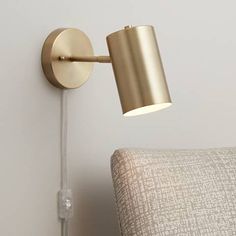 a gold wall light on a white wall next to a beige chair with a pillow