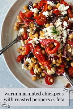 a white plate topped with vegetables and feta cheese next to a fork on a table