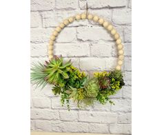 a wooden beaded wreath with succulents and greenery hangs on a brick wall