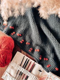 yarn and knitting needles on a table next to an orange ball of yarn with red flowers