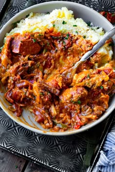 a bowl filled with meat and mashed potatoes on top of a wooden table next to a fork