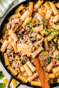 a skillet filled with pasta, meat and spinach on top of a table