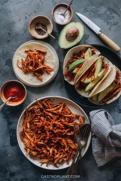 two plates filled with pulled pork tacos and avocado slices on the side