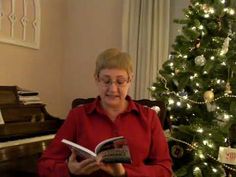 an older woman reading a book in front of a christmas tree