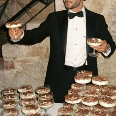 a man in a tuxedo is holding up some desserts and wine glasses