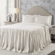 a white bed with ruffled bedspread and pillows