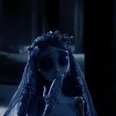 a creepy doll with long hair wearing a veil and holding a finger up to her mouth